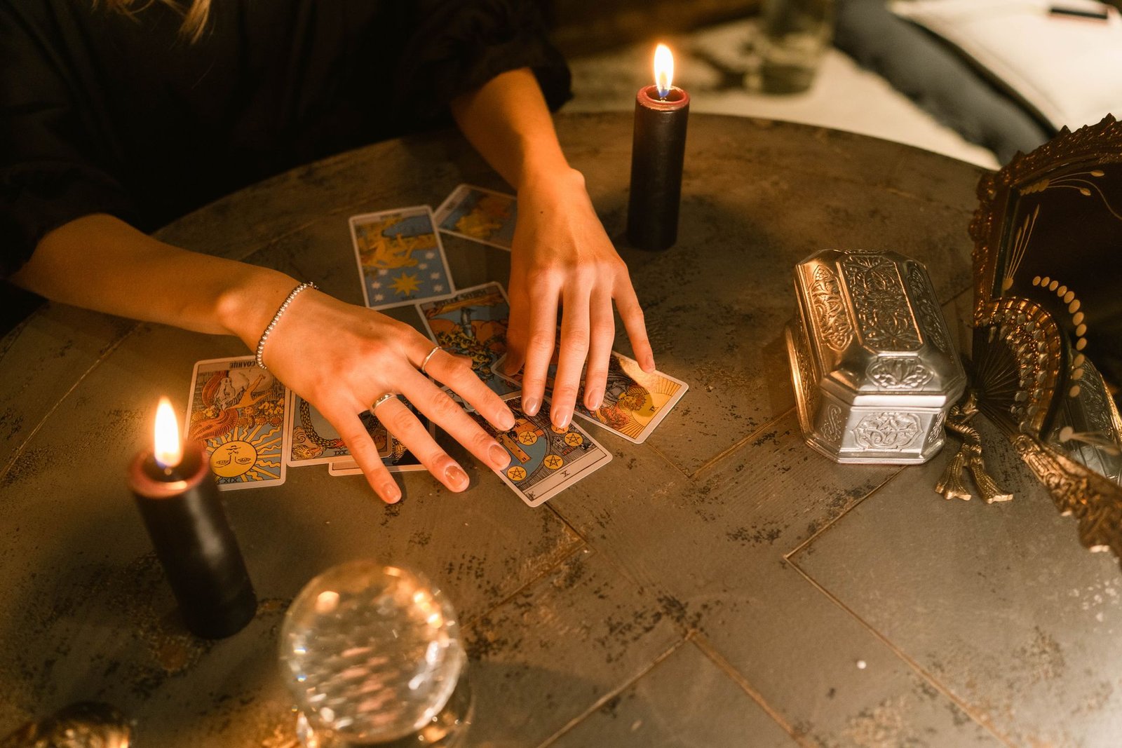 Hands laid gently over a tarot spread beside two lit candles, mid-reading